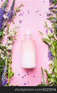 Natural cosmetic product bottle of lotion,shampoo or moisturizer with herbs and flowers on pink background, top view, copy space, vertical. Beauty, skin and hair care concept