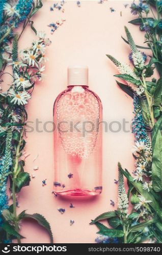 Natural Cosmetic product bottle on pink pale background with plant and flowers, top view, copy space. Floral cosmetics, botanical fragrance concept.