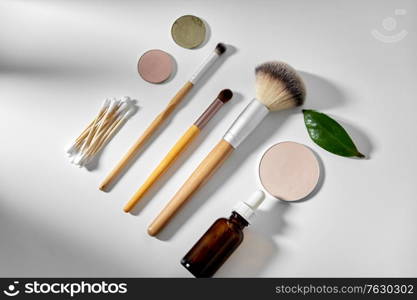 natural cosmetics and eco living concept - wooden make up brushes, cotton pads and swabs, eye shadows and essential oil or serum on white background. make up brushes, cosmetics and cotton swabs