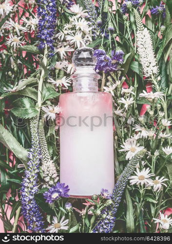 Natural cosmetics bottle with pastel pink essence, tonic, cleansing oil , emulsion or peeling on herbal leaves and wild flowers background, copy space for your text or branding , top view