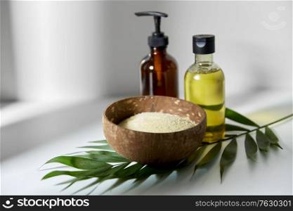 natural cosmetics, sustainability and eco living concept - sea salt in bowl, liquid soap or shower gel, massage oil and palm leaf on white background. natural cosmetics and bodycare items