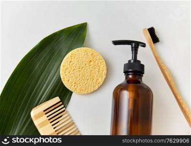 natural cosmetics, sustainability and eco living concept - wooden comb, sponge, liquid soap or shower gel and green leaf on white background. comb, sponge, liquid soap or shower gel and leaf