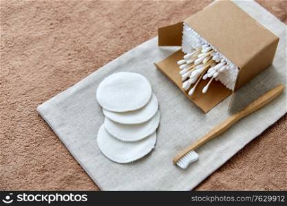 natural cosmetics, sustainability and eco living concept - wooden toothbrush, cotton pads and swabs in paper box on canvas bag and bath towel. wooden toothbrush, cotton pads and swabs in box
