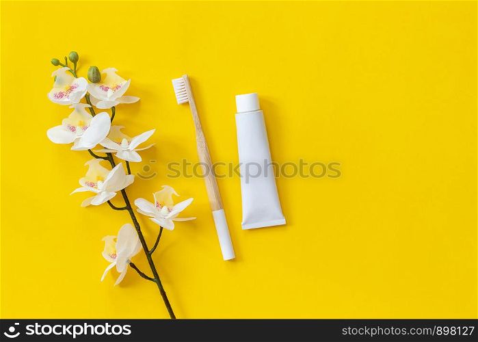 Natural eco-friendly bamboo brush, tube of toothpaste and orhid flower. Set for washing on paper yellow background. Copy space for text or your design Top view Flat lay.. Natural eco-friendly bamboo brush, tube of toothpaste and orhid flower. Set for washing on paper yellow background. Copy space for text or your design Top view Flat lay