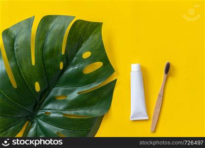 Natural eco-friendly bamboo brush, tube of toothpaste and tropical leaf monstera. Set for washing on paper yellow background. Top view Flat lay.. Natural eco-friendly bamboo brush, tube of toothpaste and tropical eaf monstera. Set for washing on paper yellow background. Top view Flat lay