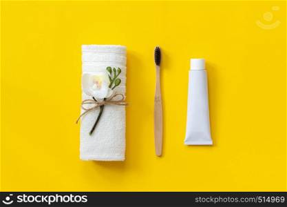 Natural eco-friendly bamboo brush, white towel and tube of toothpaste. Set for washing on paper yellow background. Copy space for text or your design Top view Flat lay.. Natural eco-friendly bamboo brush, white towel and tube of toothpaste. Set for washing on paper yellow background. Copy space for text or your design Top view Flat lay