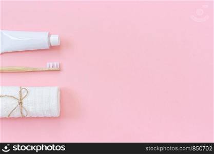 Natural eco-friendly bamboo brush, white towel and tube of toothpaste. Set for washing and brushing your teeth on pink background. Template for design Top view Flat lay Copy space.. Natural eco-friendly bamboo brush, white towel and tube of toothpaste. Set for washing and brushing your teeth on pink background. Template for design Top view Flat lay Copy space