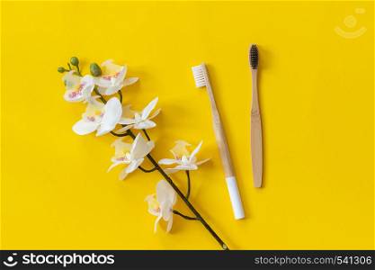 Natural eco-friendly bamboo brushes and orhid flower on paper yellow background. Copy space for text or your design Top view Flat lay.. Natural eco-friendly bamboo brushes and orhid flower on paper yellow background. Copy space for text or your design Top view Flat lay