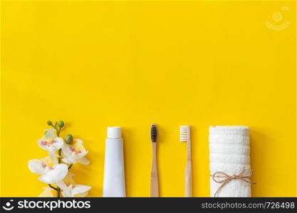 Natural eco-friendly bamboo brushes, white towel, tube of toothpaste and orchid flower. Set for washing on paper yellow background. Copy space for text or your design Top view Flat lay.. Natural eco-friendly bamboo brushses e towel and tube of toothpaste and orhid flower for washing on paper yellow background. Copy space for text or your design Top view Flat lay