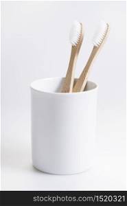 natural eco friendly toothbrush with wooden bamboo handle in a white cup on white background.