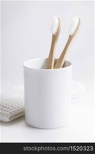 natural eco friendly toothbrush with wooden bamboo handle in a white cup on white background.