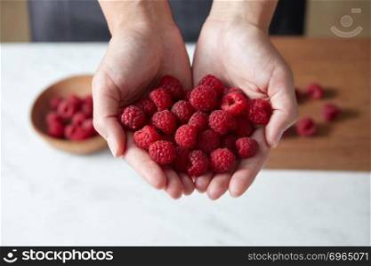 Natural fresh home grown fruits in the girls’ hands. Ingredients for delicious desserts on kitchen table. Concept healthy food.. Freshly picked red raspberry for cooking homemade fruits pie. A woman prepares berries above white table.
