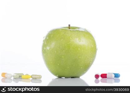 Natural green apple and various pills on white background. Green apple and various colored pills on white background
