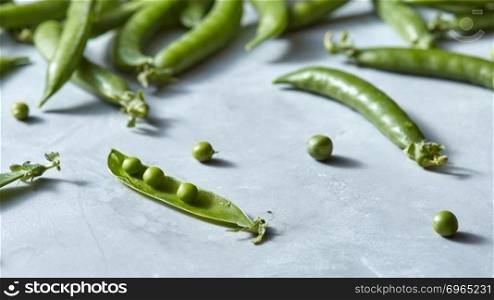Natural green vegetables - pods of green peas with small spherical seed on a gray with copy space. Detox food concept.. Organic green pods of young green peas opened on a gray marble table.