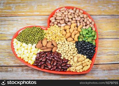 Natural healthy food for cooking ingredients collage various beans mix peas agriculture / Set of different whole grains beans and legumes seeds lentils and nuts colorful on red heart background