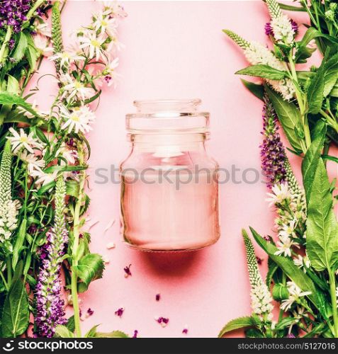 Natural herbal skin care cosmetic concept. Glass jar with cream and fresh herbs and flowers on pink background, top view, copy space, square. Beauty, skin and hair care concept