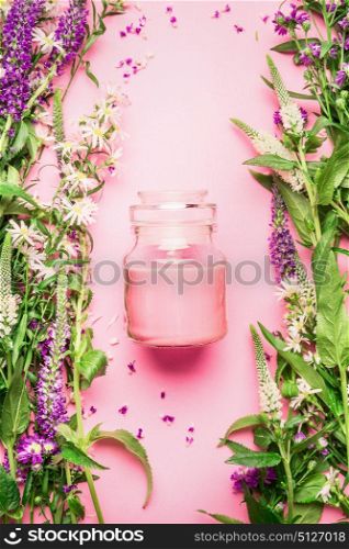 Natural herbal skin care cosmetic concept. Glass jar with cream or lotion and fresh herbs and flowers on pink background, top view, copy space, vertical. Beauty, skin and hair care concept