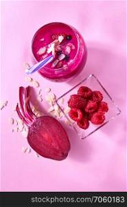Natural ingredients for healthy smoothie from red vegetables and fruits, nuts in glass on pink. Concept of vegan and healthy eating.. Fresh juicy detox smoothies in glass cup with red berries, beetroot, almonds on a pink paper background. Top view.