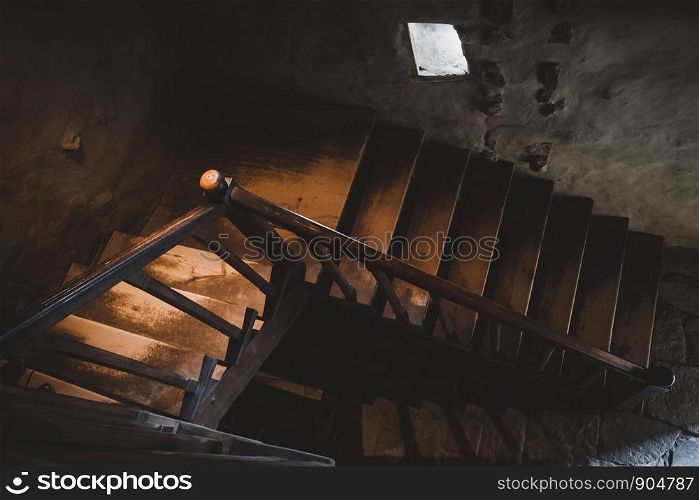 Natural light lit old style wooden stairs with handrail in the dark.