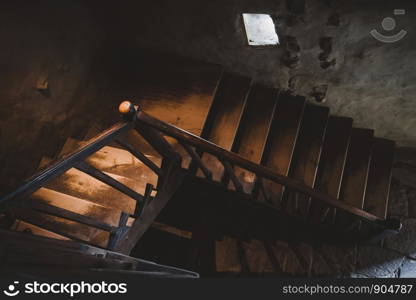 Natural light lit old style wooden stairs with handrail in the dark.