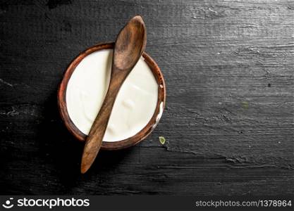 Natural milk yogurt in a bowl with a spoon. On the black chalkboard.. Natural milk yogurt in a bowl with a spoon.