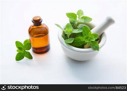 Natural Mint Essential Oil in a Glass Bottle with Fresh Mint Leaves in white porcelain mortar.