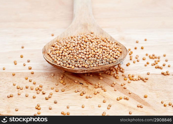 Natural mustard seeds on a wooden serving spoon on wooden board with selective focus