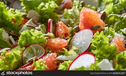 Natural organic close-up background with fresh vegetables, citrus fruits, seeds. Concept of helthy detox dieting.. Freshly picked greens in the vegetarian salad - lettuce, slices of radish, grapefruit, cheese, pumpkin seeds.