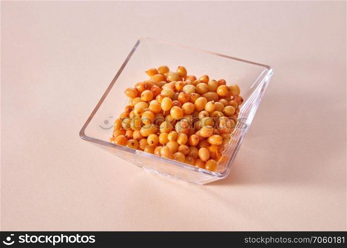 Natural organic fruits, natural ripe juicy yellow berries in the glass bowl on a paper background.. Yellow ripe sweet berries - sea buckthorn in the glass bowl on a beige paper background.