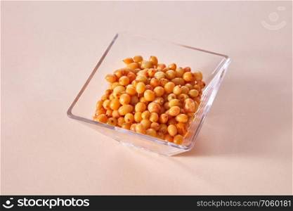 Natural organic fruits, natural ripe juicy yellow berries in the glass bowl on a paper background.. Yellow ripe sweet berries - sea buckthorn in the glass bowl on a beige paper background.