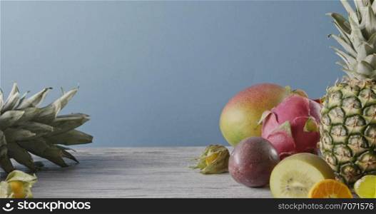 Natural organic tropical exotic fruits on a wooden table on a blue background. . Dolly out motion, 4K video, 3840, 2160p. Concept of vegetarian diet eating.. Summer healthy exotic passion fruits, pine apples and dragon fruit on a gray wooden table on a blue. Vegetarian healthy concept. Dolly out motion, 4K video, 3840, 2160p.