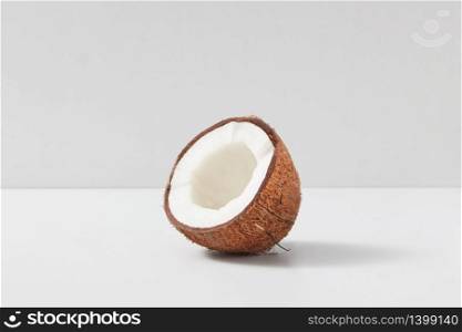 Natural organic tropical fruit half of ripe coconut on a light grey duotone background, copy space. Vegetarian concept.. Half of fresh ripe tropical coconut fruits on light grey background.