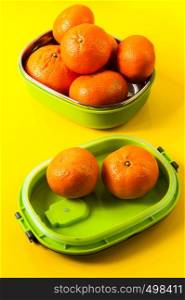 natural tangerines in a green lunch box on a yellow background