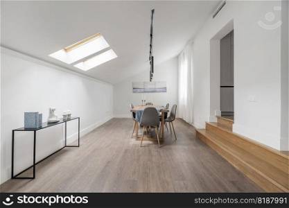 Natural wood dining table in the living room of an attic apartment with wooden steps and skylights in the ceiling