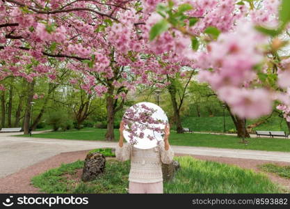 nature and people concept - woman holding round mirror with cherry tree reflection in spring garden or park. woman with cherry tree reflection in round mirror