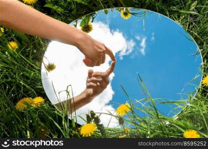 nature concept - hand touching sky reflection in round mirror on summer field. hand touching sky reflection in mirror on field