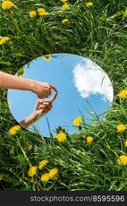 nature concept - hand touching sky reflection in round mirror on summer field. hand touching sky reflection in mirror on field