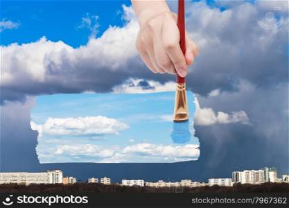 nature concept - seasons and weather changing: hand with paintbrush paints blue sky with white clouds instead of rain over city
