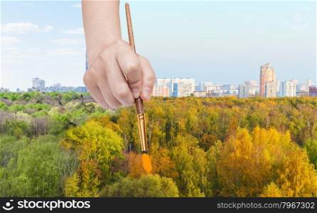 nature concept - seasons and weather changing: hand with paintbrush paints yellow autumn forest from green