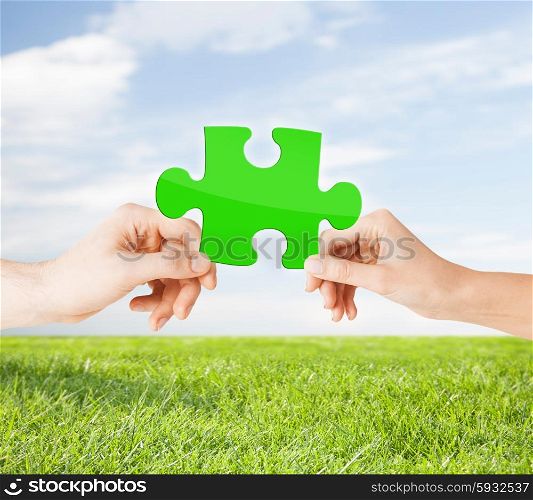 nature, ecology, energy saving, people and environment concept - close up of couple hands with green puzzle over blue sky and grass background