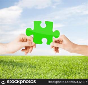 nature, ecology, energy saving, people and environment concept - close up of couple hands with green puzzle over blue sky and grass background