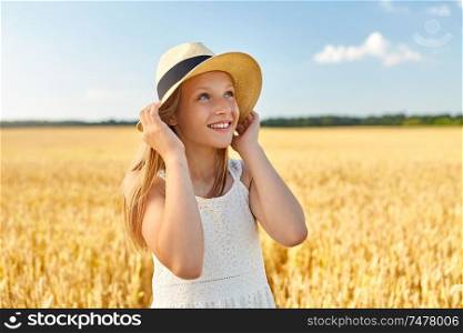 nature, fashion and people concept - portrait of smiling young girl in straw hat on cereal field in summer. portrait of girl in straw hat on field in summer