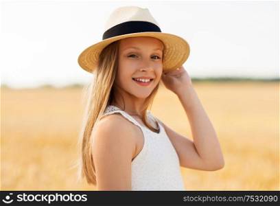 nature, fashion and people concept - portrait of smiling young girl in straw hat on cereal field in summer. portrait of girl in straw hat on field in summer