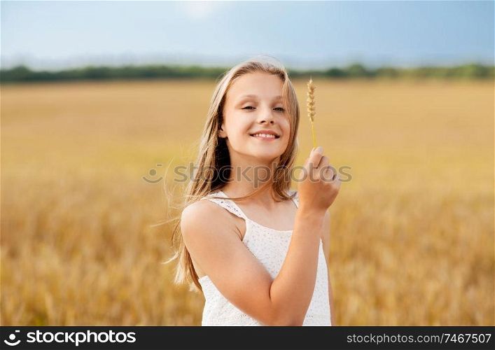 nature, harvesting and eco concept - smiling young girl holding spikelet of wheat on cereal field in summer. girl with spikelet of wheat on cereal field