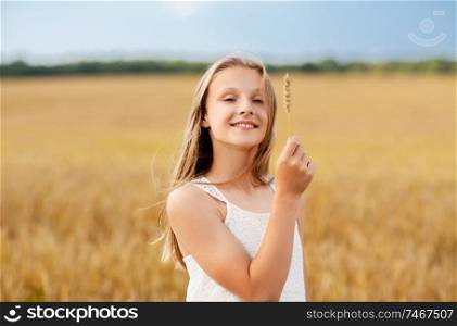 nature, harvesting and eco concept - smiling young girl holding spikelet of wheat on cereal field in summer. girl with spikelet of wheat on cereal field