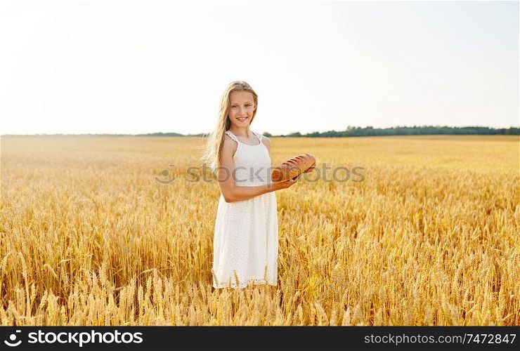 nature, healthy eating and harvesting concept - smiling young girl holding loaf of white bread on cereal field in summer. girl with loaf of white bread on cereal field