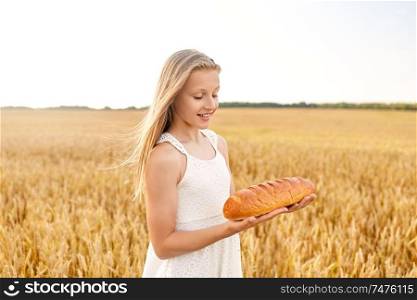 nature, healthy eating and harvesting concept - smiling young girl holding loaf of white bread on cereal field in summer. girl with loaf of white bread on cereal field
