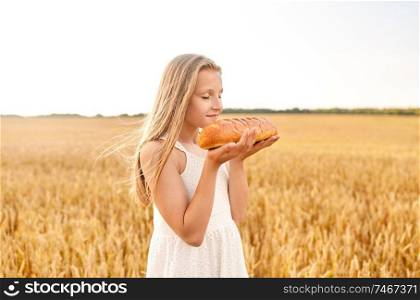 nature, healthy eating and harvesting concept - smiling young girl smelling loaf of white bread on cereal field in summer. girl smelling loaf of white bread on cereal field