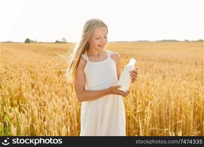 nature, healthy eating and organic concept - smiling young girl holding bottle of milk on cereal field in summer. happy girl with bottle of milk on cereal field