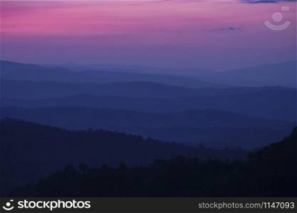 Nature landscape background beautiful view of the morning fog filling the valleys of smooth hills mountain range layer dark blue forest sunrise and sunset in mountains with purple sky dramatic